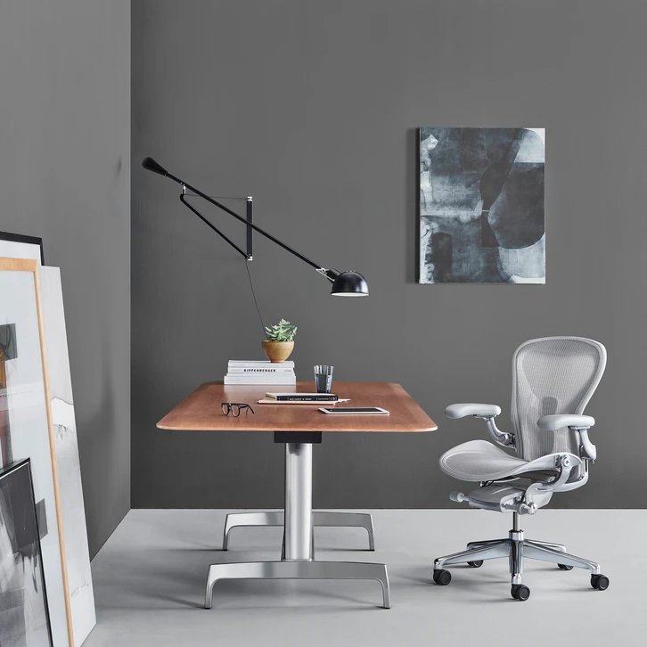 Bureau ergonomique en bois de noyer sur pied central réglable en hauteur, chaise Herman Miller Aeron grise, lampe articulée murale noire style Anglepoise